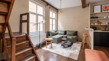 A modern living space with a staircase, a sectional sofa, a coffee table, and a kitchen area with shelves.