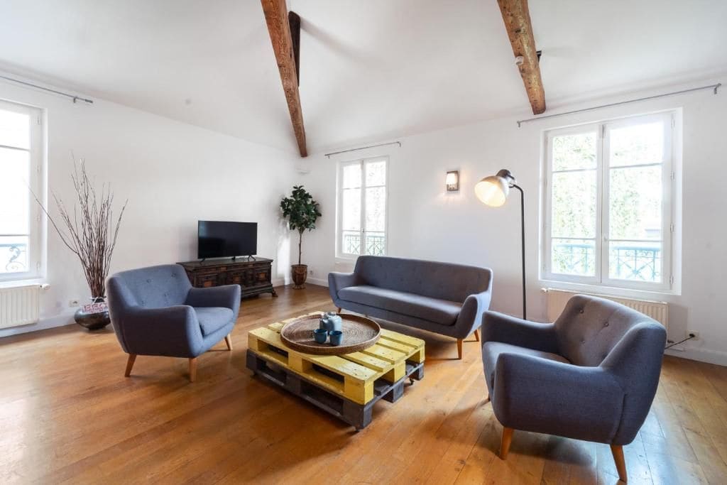 Un salón comedor espacioso con suelos de madera, un sofá gris, un sillón azul y una mesa de centro de madera.