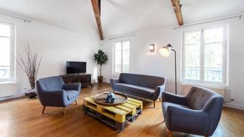 Un salón comedor espacioso con suelos de madera, un sofá gris, un sillón azul y una mesa de centro de madera.