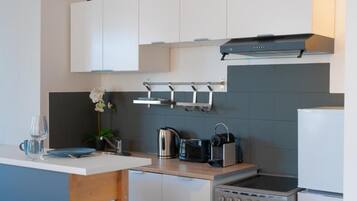 A modern kitchen with white cabinets, a stainless steel kettle, a toaster, and a built-in oven.