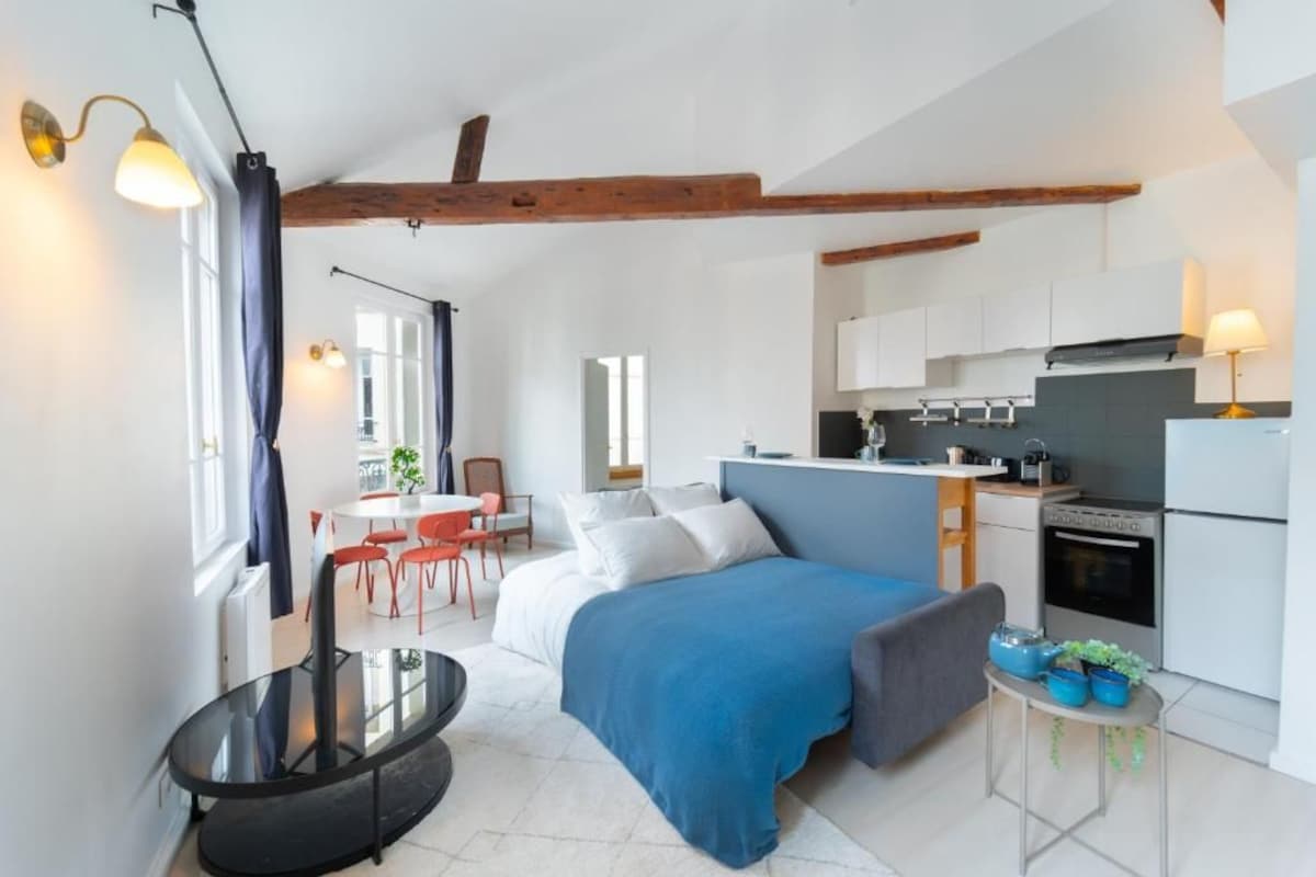 Un dormitorio compacto con cama, mesita de noche y una pequeña cocina con estufa y armarios.