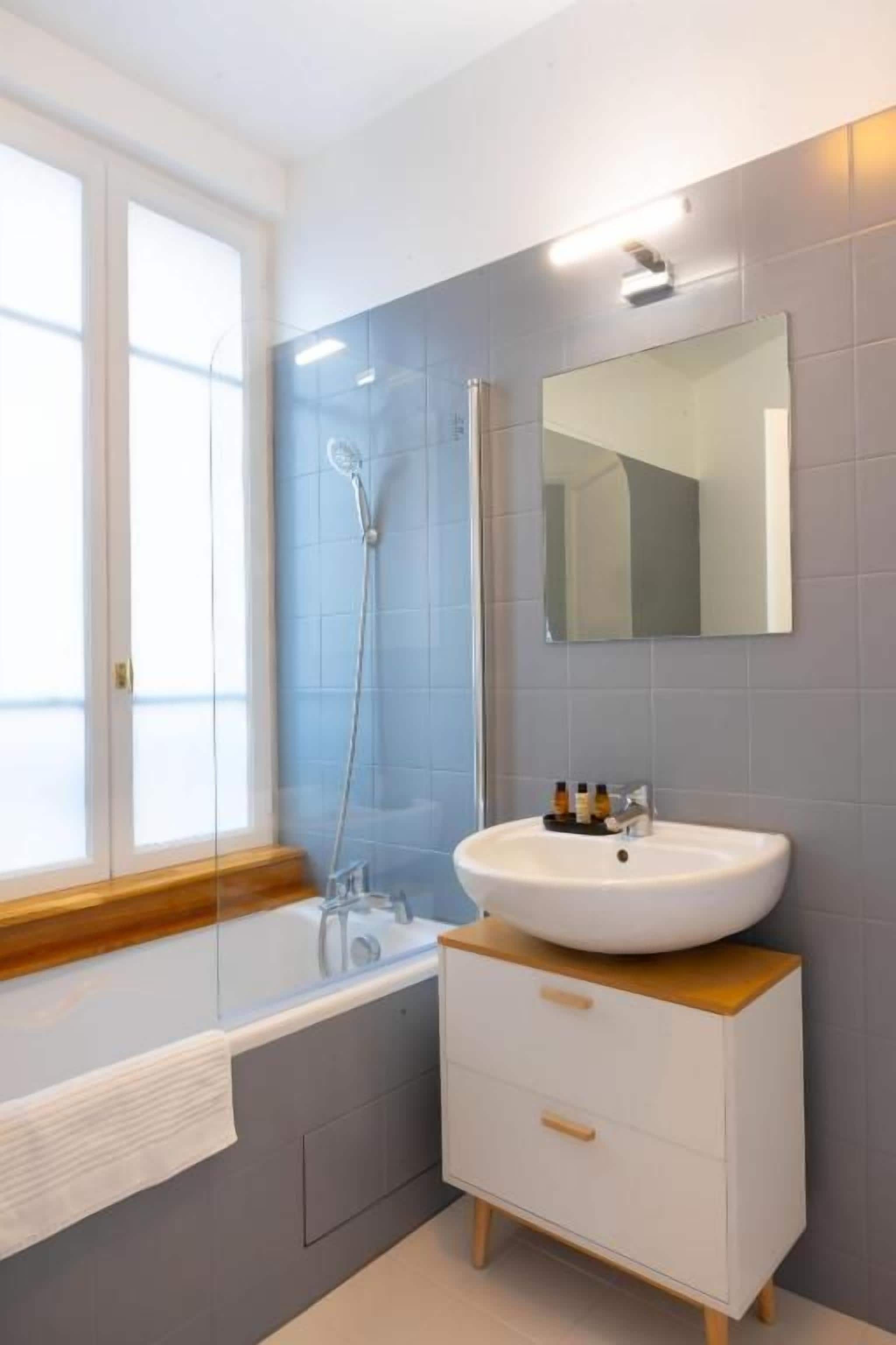 Un baño moderno con una bañera, un tocador blanco con cajones y un espejo sobre el lavabo.
