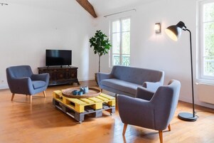 Una sala de estar con un sofá, dos sillones, una mesita de centro, un televisor y una lámpara de pie.