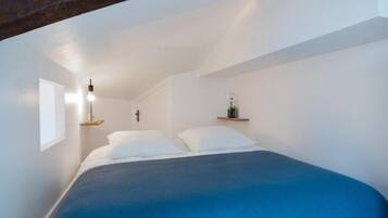 A bedroom with a bed, a hanging light fixture, and a small shelf with a plant.