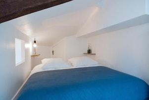 Un dormitorio con una cama, una lámpara colgante y una pequeña estantería con una planta.