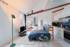 Una habitación pequeña con cama, mesita de noche y vista a la cocina.
