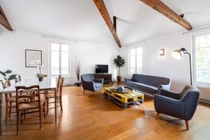 Un amplio salón con suelo de madera, una mesa de comedor con sillas, un sofá y un televisor.