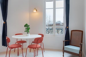 Una habitación con una mesa redonda, seis sillas rojas, una planta en maceta, una silla de madera y un ventanal con cortinas.