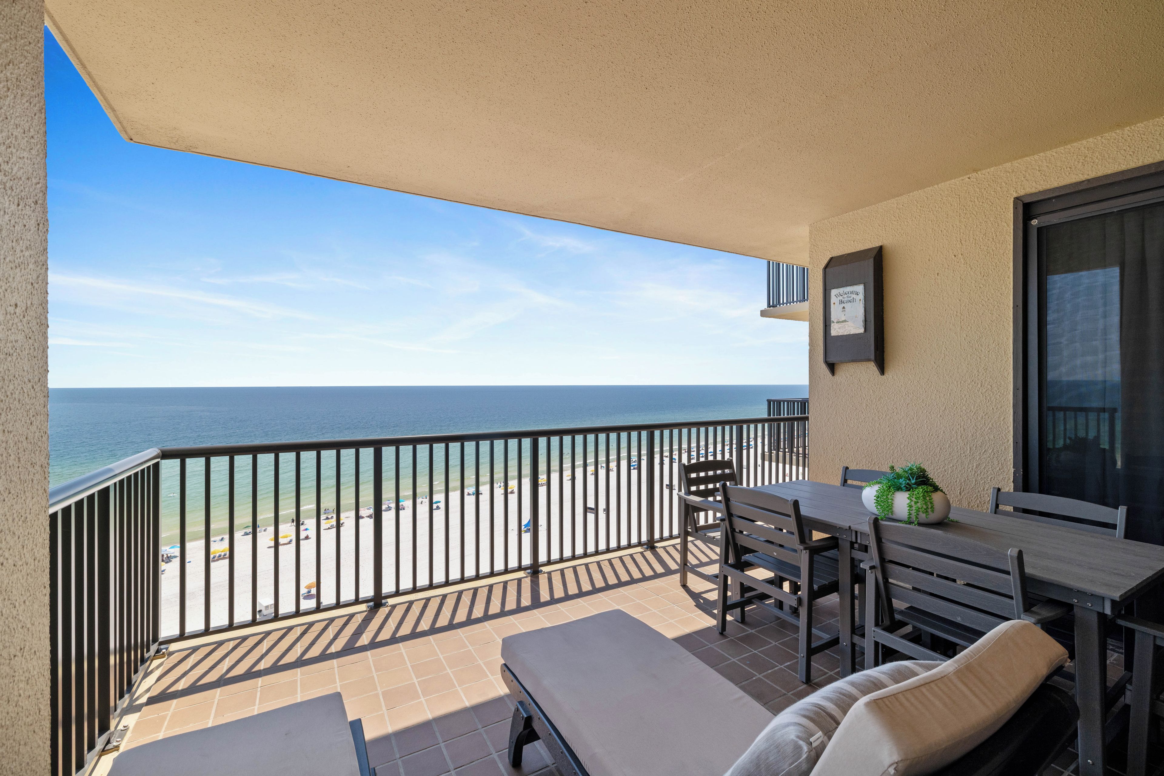Een balkon met uitzicht op het strand, een tafel met stoelen en een bloempot.