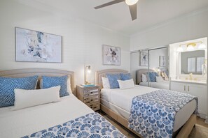 A hotel room with two beds, a bedside table with a lamp, a large mirror, and artwork on the walls. - Romar House 1004A by Liquid Life (Orange Beach)