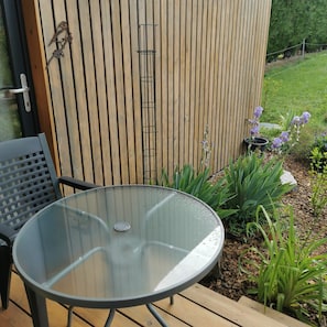 A glass-top table with metal legs, a black chair, and a wooden deck.