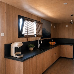 A modern kitchen with a built-in Bosch coffee maker, a black countertop, a wooden cabinet, a window with blinds, and a wall-mounted light fixture.