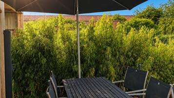 Une terrasse extérieure avec une table et des chaises, un grand parasol et une plateforme en bois.