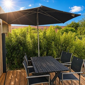 En udendørs terrasse med et bord, stole og en stor parasol, samt et trægulv.