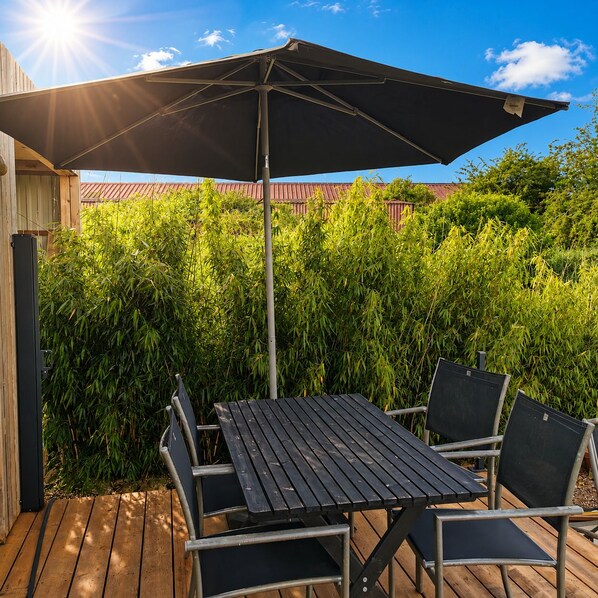 An outdoor patio with a table and chairs, a large umbrella, and a wooden deck.