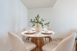 A dining table set with white plates, bowls, and glasses, surrounded by beige chairs. - Resort-Living 2BR+Maids and Beach Access, Close to Khor Fakkan Amphitheatre (Khor Fakkan)