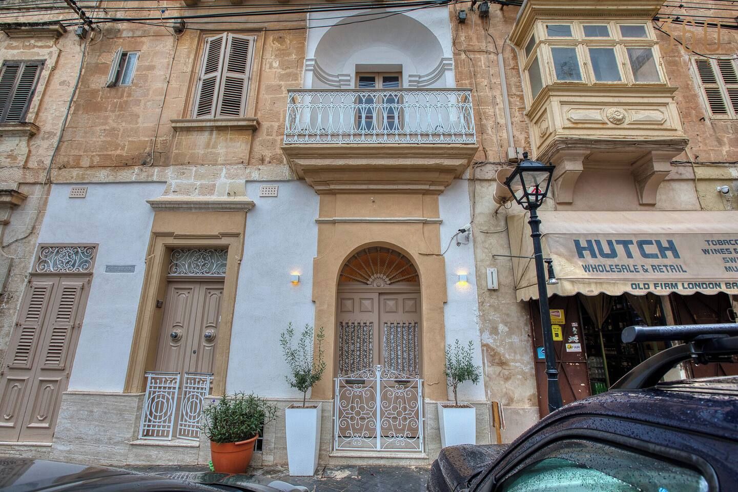 A building with a traditional facade, a balcony with ornate metal railings, and a storefront with signage for 'Hutch Wholesale & Retail'.