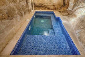 Et rektangulært pool med blå mosaikfliser, omgivet af stenvægge.