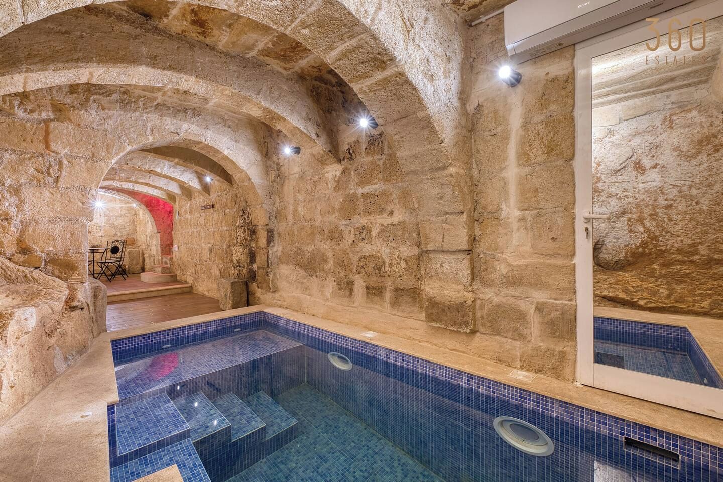 A stone-walled indoor pool with a tiled floor and steps leading to a seating area.