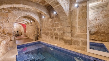 A stone-walled indoor pool with a tiled floor and steps leading to a seating area.