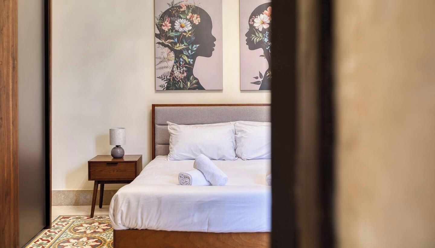 Una camera da letto con un letto, un comodino, una lampada e due opere d'arte floreali alle pareti.
