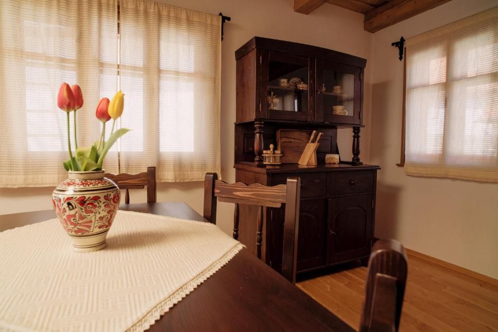 A dining area with a table set for two, a vase with flowers, and a wooden cabinet with glass doors.