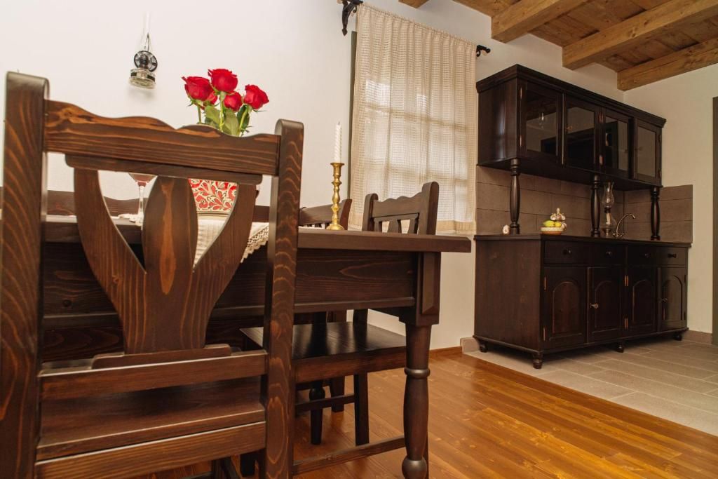 A wooden dining table with chairs, a dark wooden cabinet, and a vase with red flowers.