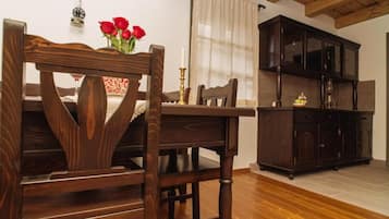 A wooden dining table with chairs, a dark wooden cabinet, and a vase with red flowers.