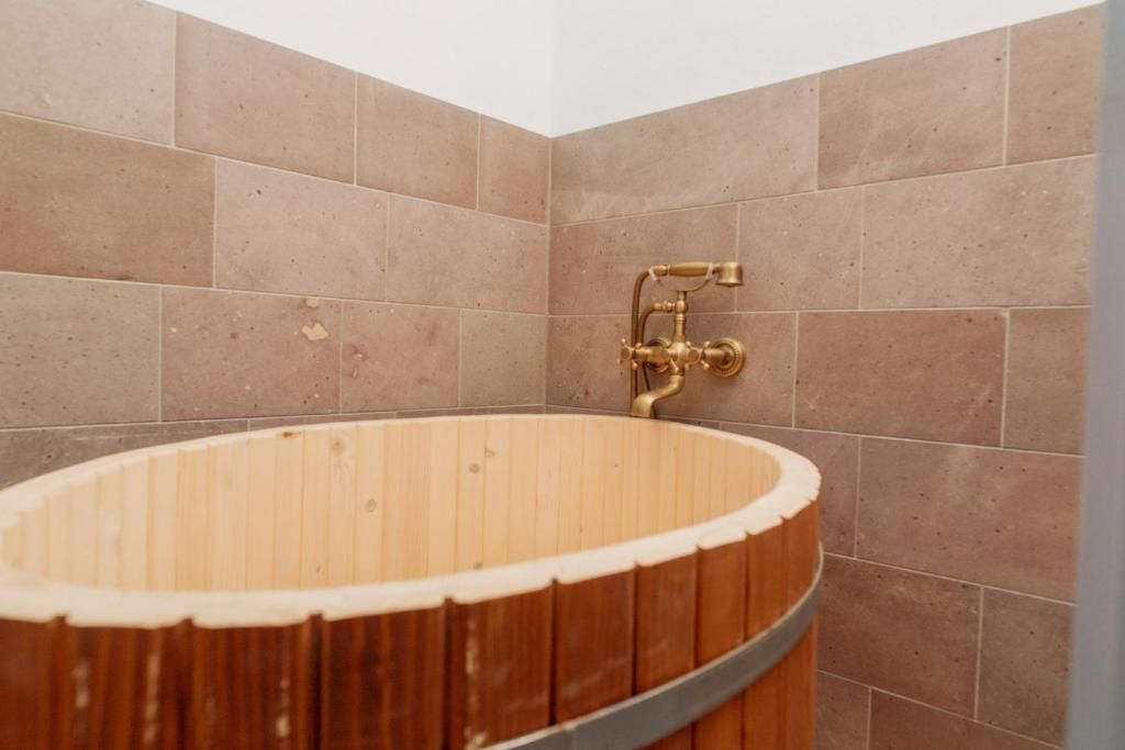 A wooden bathtub with a faucet in a corner of a room with tiled walls.