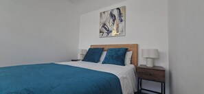 A bedroom with a bed, two pillows, a nightstand with a lamp, and a painting on the wall. - Deluxe one-bed apartment in Yaxley near A1 (Yaxley)