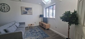 A modern living room with a grey sofa, a blue rug, a small table, a TV stand, and a plant. - Deluxe one-bed apartment in Yaxley near A1 (Yaxley)