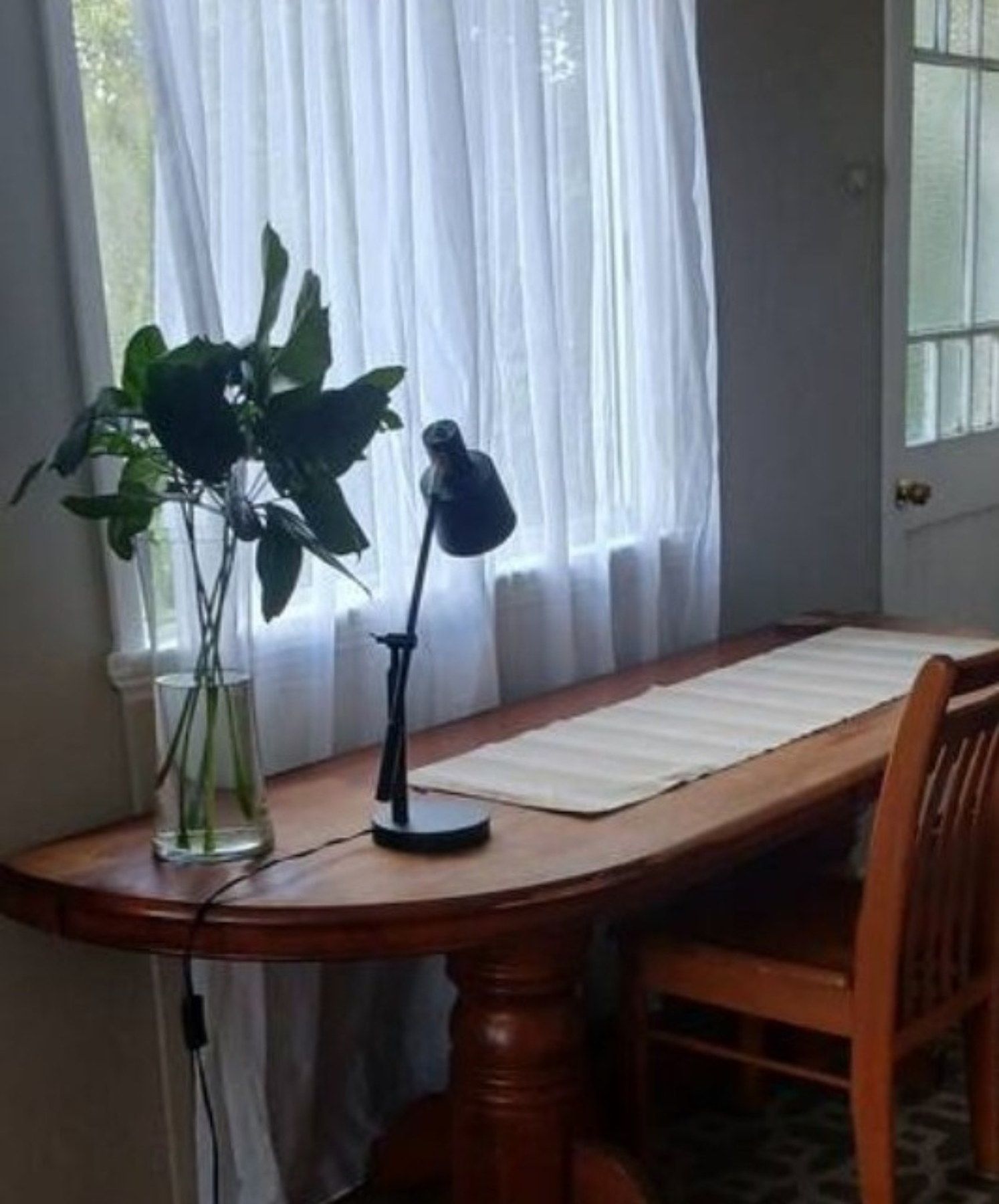 Une table à manger ornée d’un vase de plantes vertes, d’une lampe et d’une chaise.