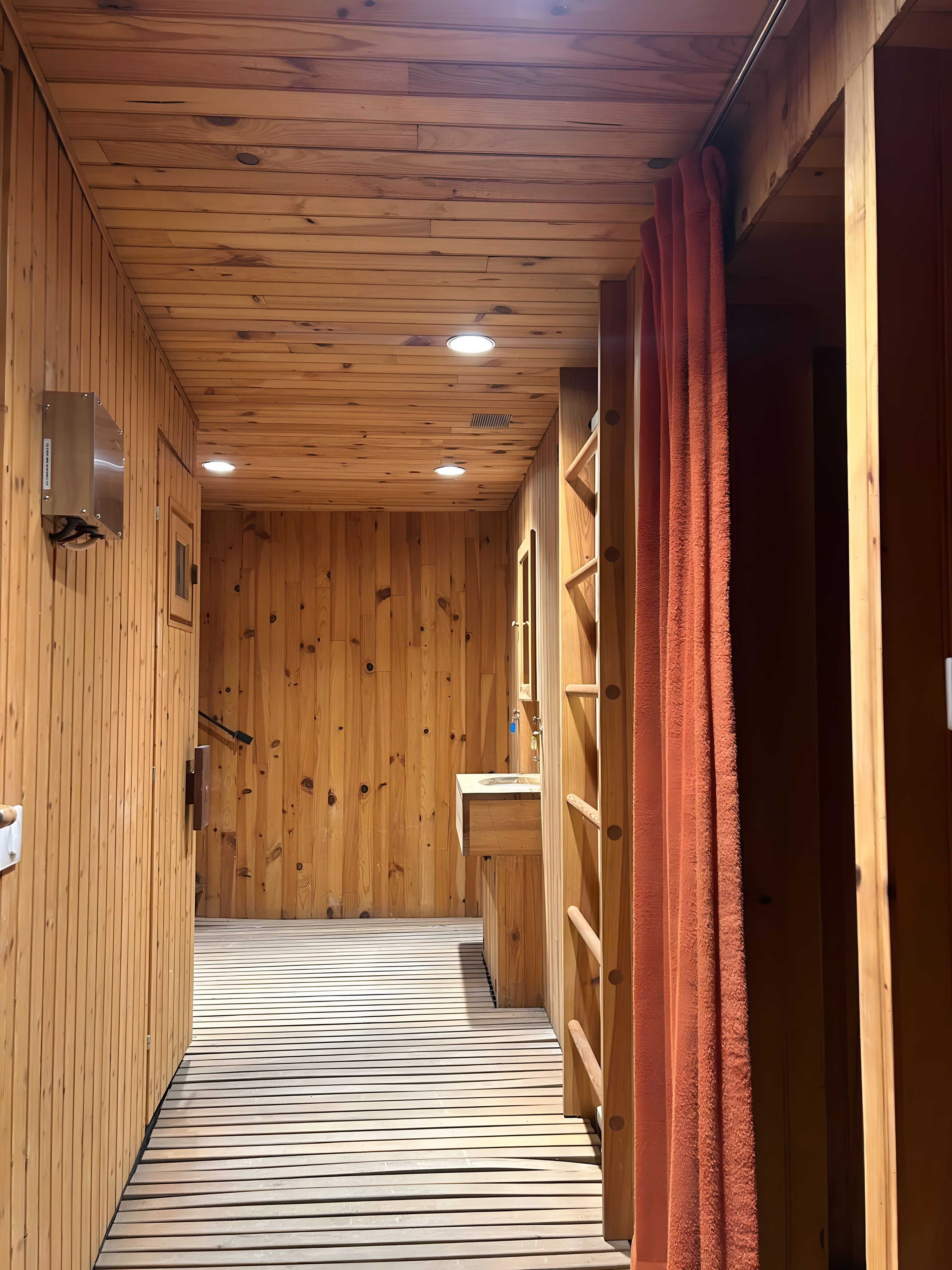 A wooden interior with a corridor leading to a room, a sink, and a shower area.