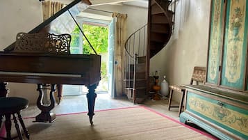 Un piano de cola en una habitación con una escalera, un mueble grande con diseños florales y vistas al exterior con follaje.