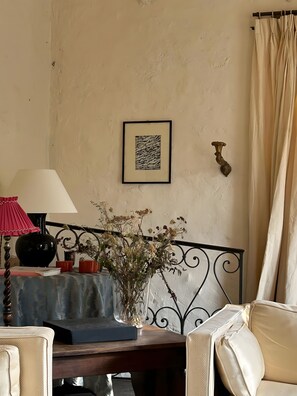 Una habitación con una cama, una mesita de noche con lámpara, un cuadro enmarcado y un jarrón con flores.