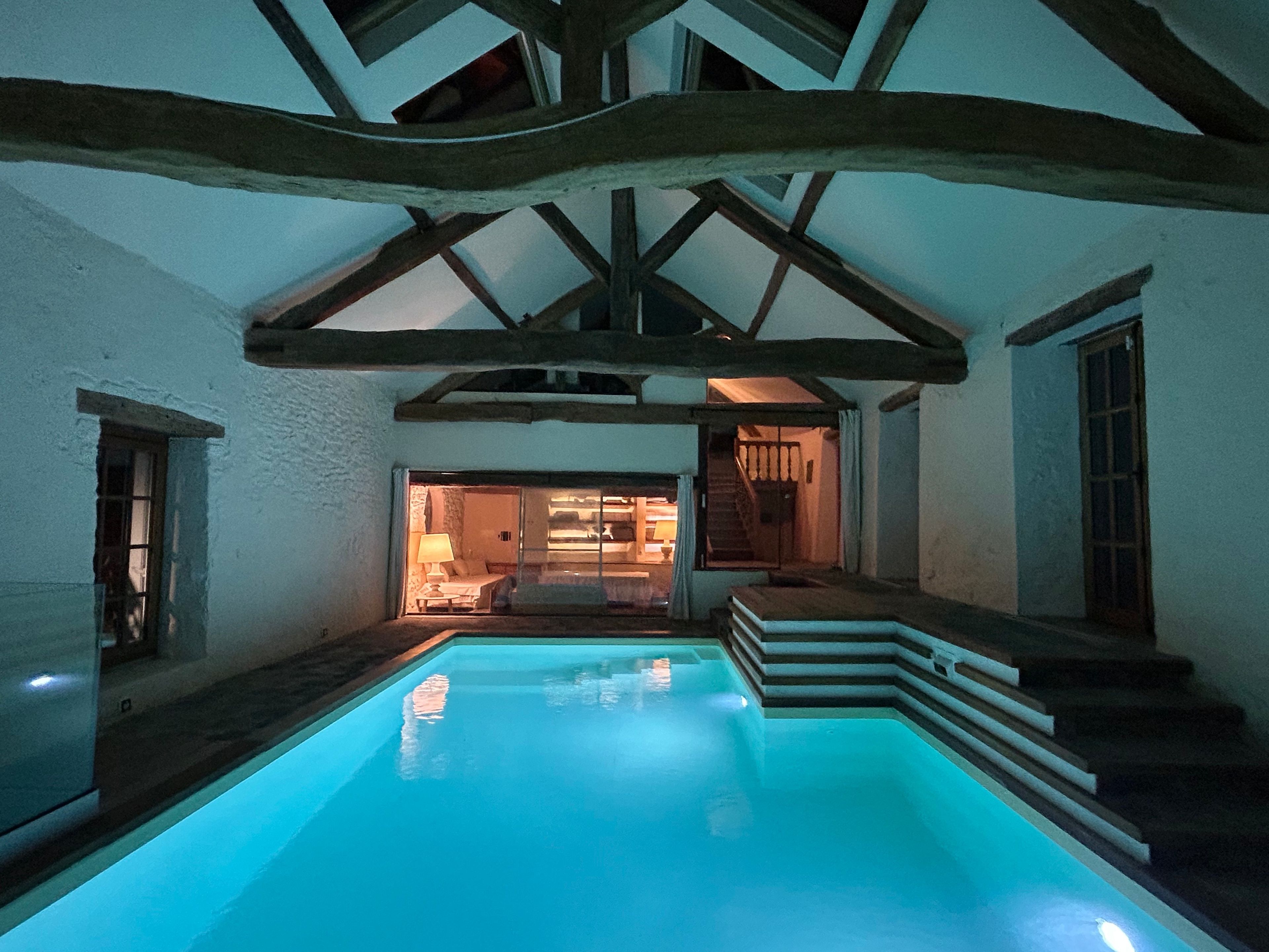 Ein Schwimmbecken mit Holzterrasse und Stufen, die zu einem Raum mit Bett und Lampe führen.