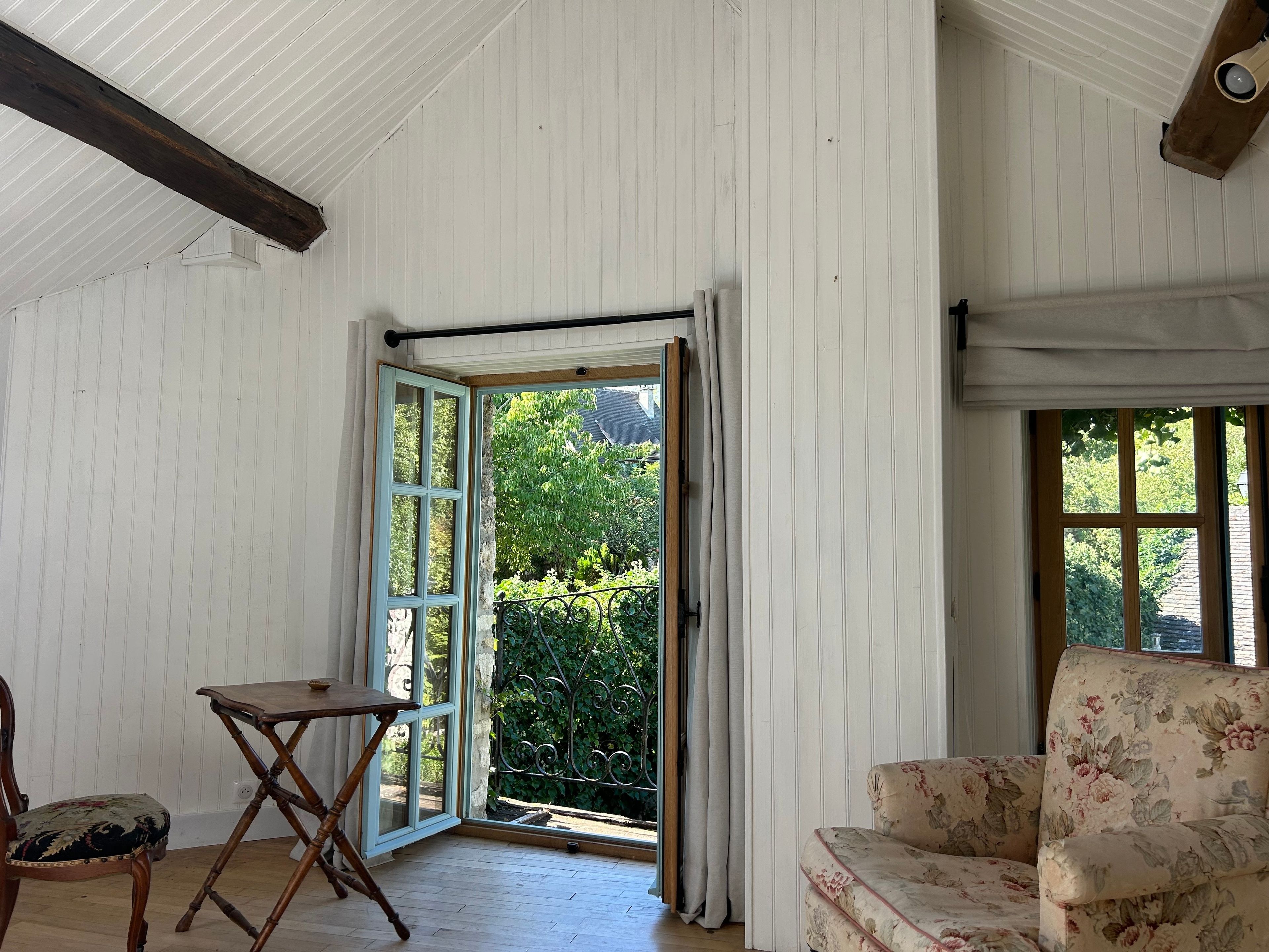 Une pièce avec un plancher en bois, une chaise, une petite table et une fenêtre donnant sur un paysage verdoyant.
