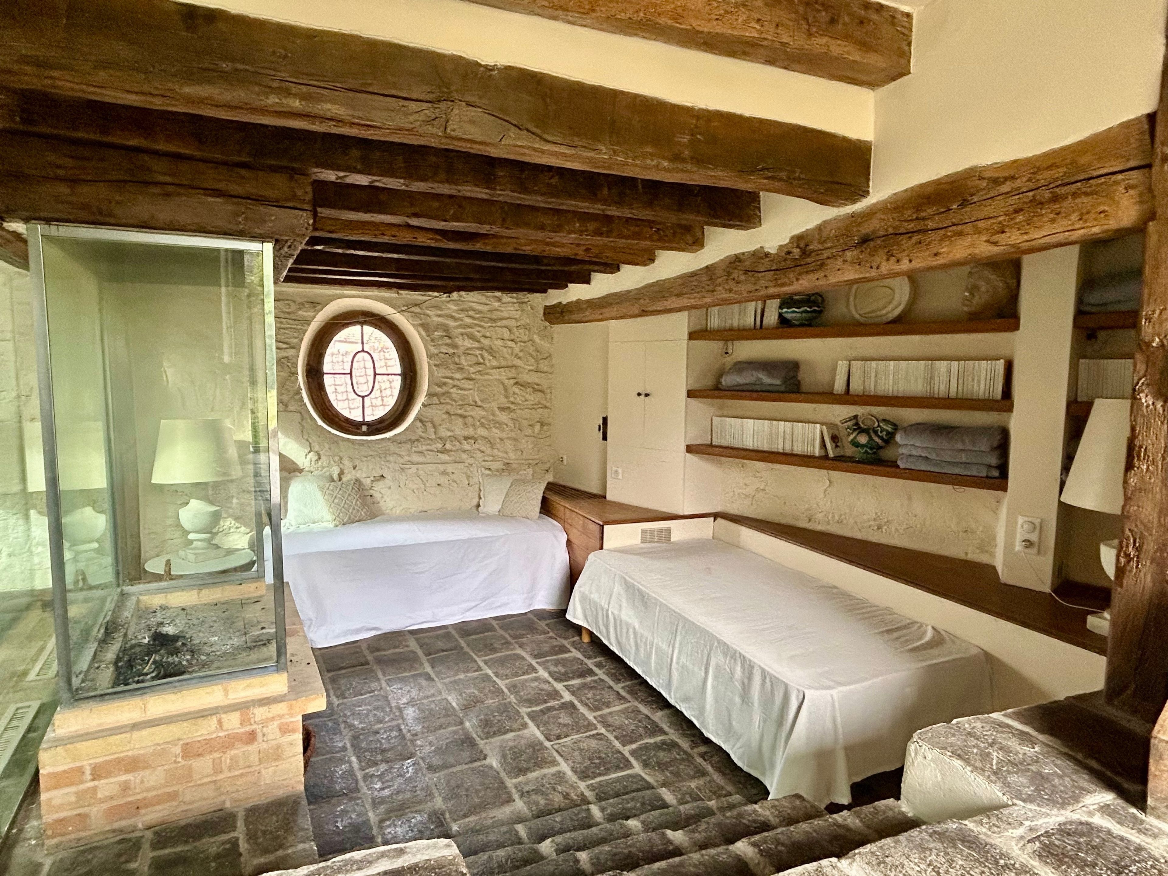 Une pièce rustique avec un mur en pierre, des poutres en bois, un lit, une petite table et une étagère avec des serviettes.