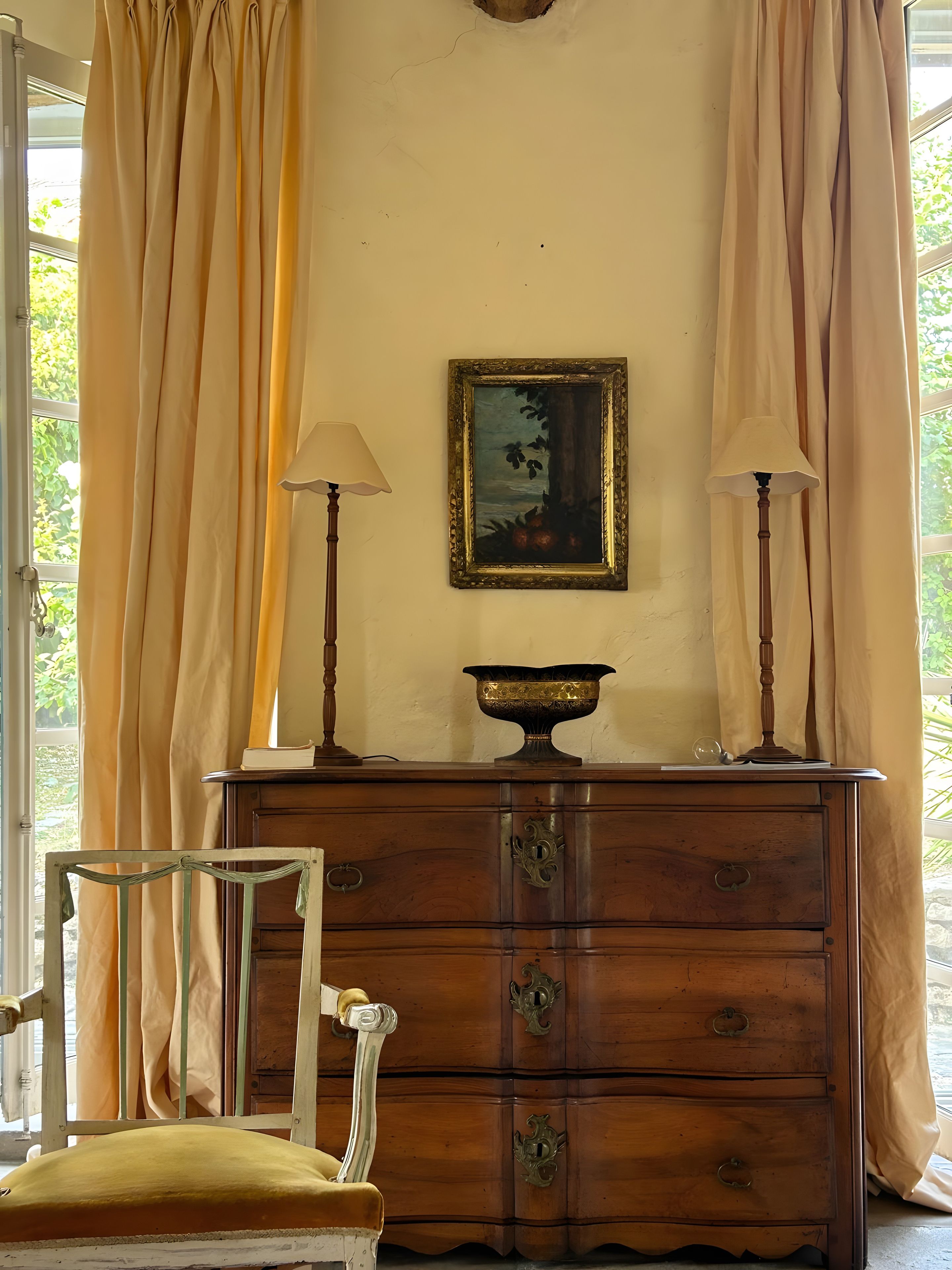 Una habitación con un aparador de madera, dos lámparas, un cuadro enmarco y una silla.