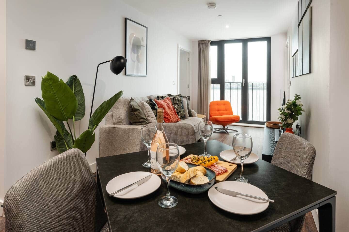 A modern dining area with a table set for two, featuring a bottle of wine, glasses, and a plate of food.