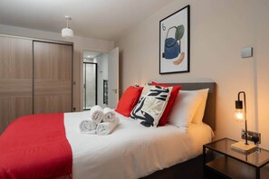 A hotel room with a bed, a bedside table with a lamp, a door, and a wall-mounted artwork. - River View 2 Bed/2 Bath Flat - Nr Everton Stadium (Liverpool)