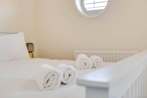A neatly made bed with rolled white towels, a white headboard, and a round window in the background. - Spacious 4-Bed Marina Home, Parking, Near City (Liverpool)
