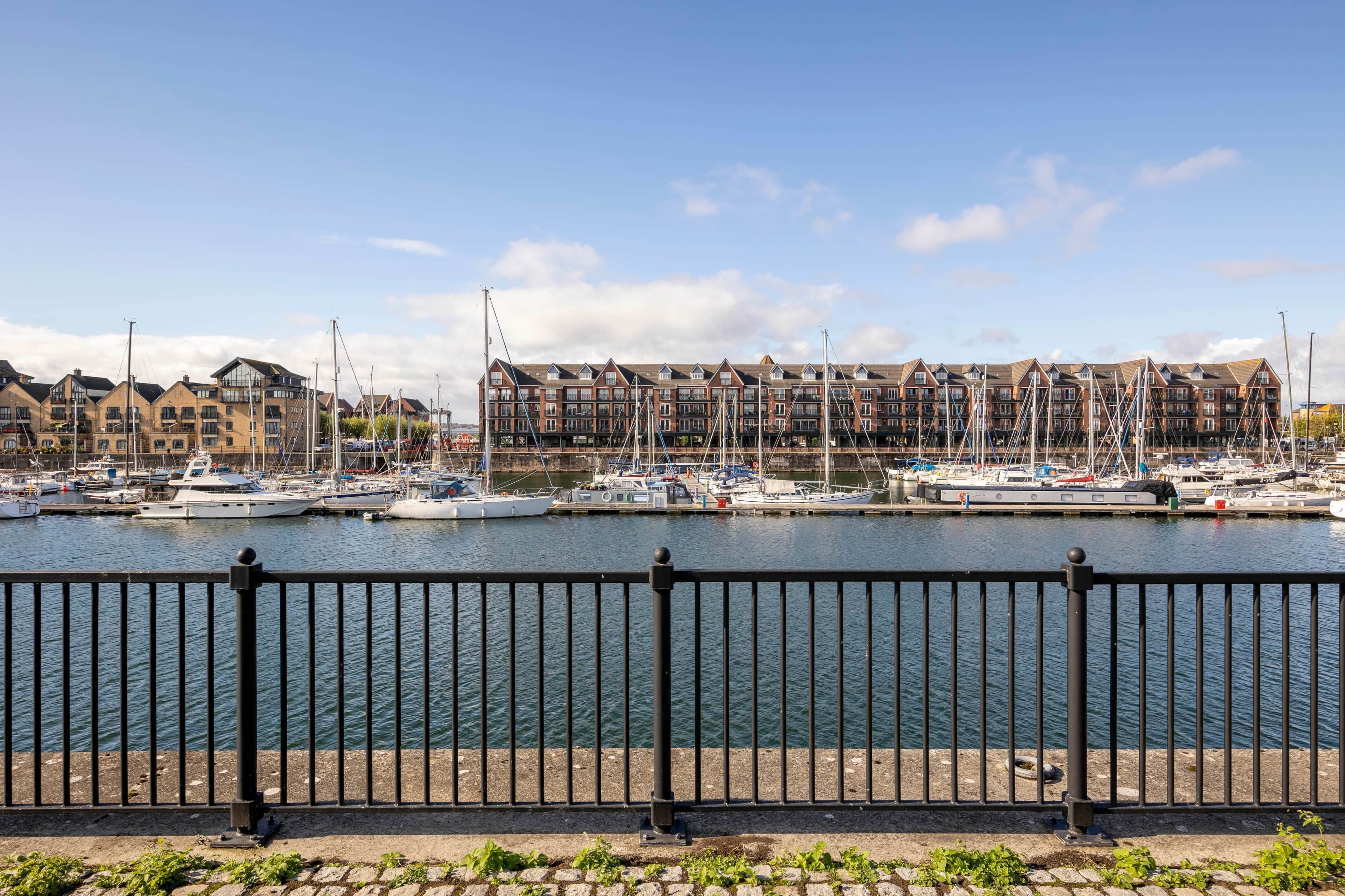 A marina with boats docked, a waterfront promenade, and residential buildings in the background.