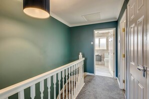 A hallway with a white railing, teal walls, and a carpeted floor leading to a door. - Spacious 4-Bed Marina Home, Parking, Near City (Liverpool)