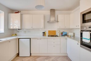 A modern kitchen with white cabinetry, a built-in oven, a microwave, and a small refrigerator. - Spacious 4-Bed Marina Home, Parking, Near City (Liverpool)