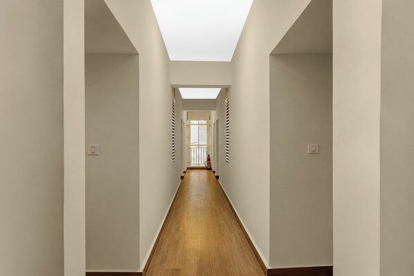 Un largo pasillo estrecho con piso de madera y paredes blancas, que conduce a una habitación con un ventanal.