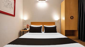 Quarto de hotel com cama, mesa de cabeceira, abajur e um quadro na parede.