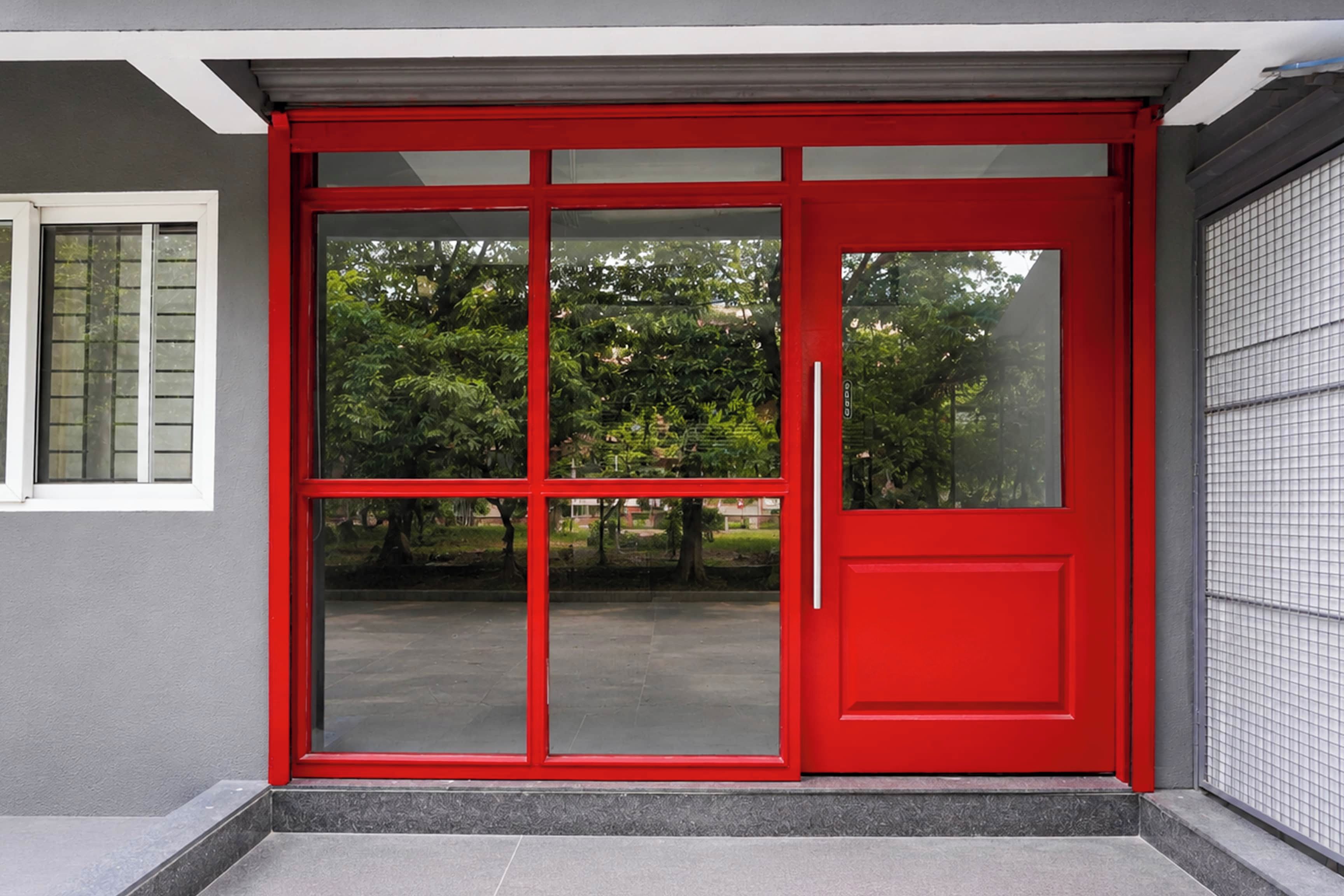 A red door with a sliding glass panel, a small window to the left, and a tiled wall to the right.