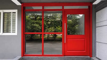 A red door with a sliding glass panel, a small window to the left, and a tiled wall to the right.