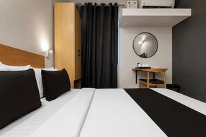 A hotel room with a bed, a bedside table, a mirror, and a small desk with a chair.